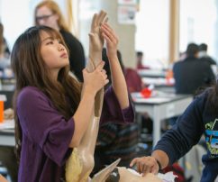 female student examining a mannequin arm in a workshop classroom