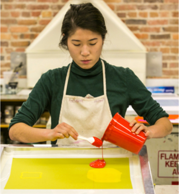 student pouring red liquid onto yellow paper in an art studio