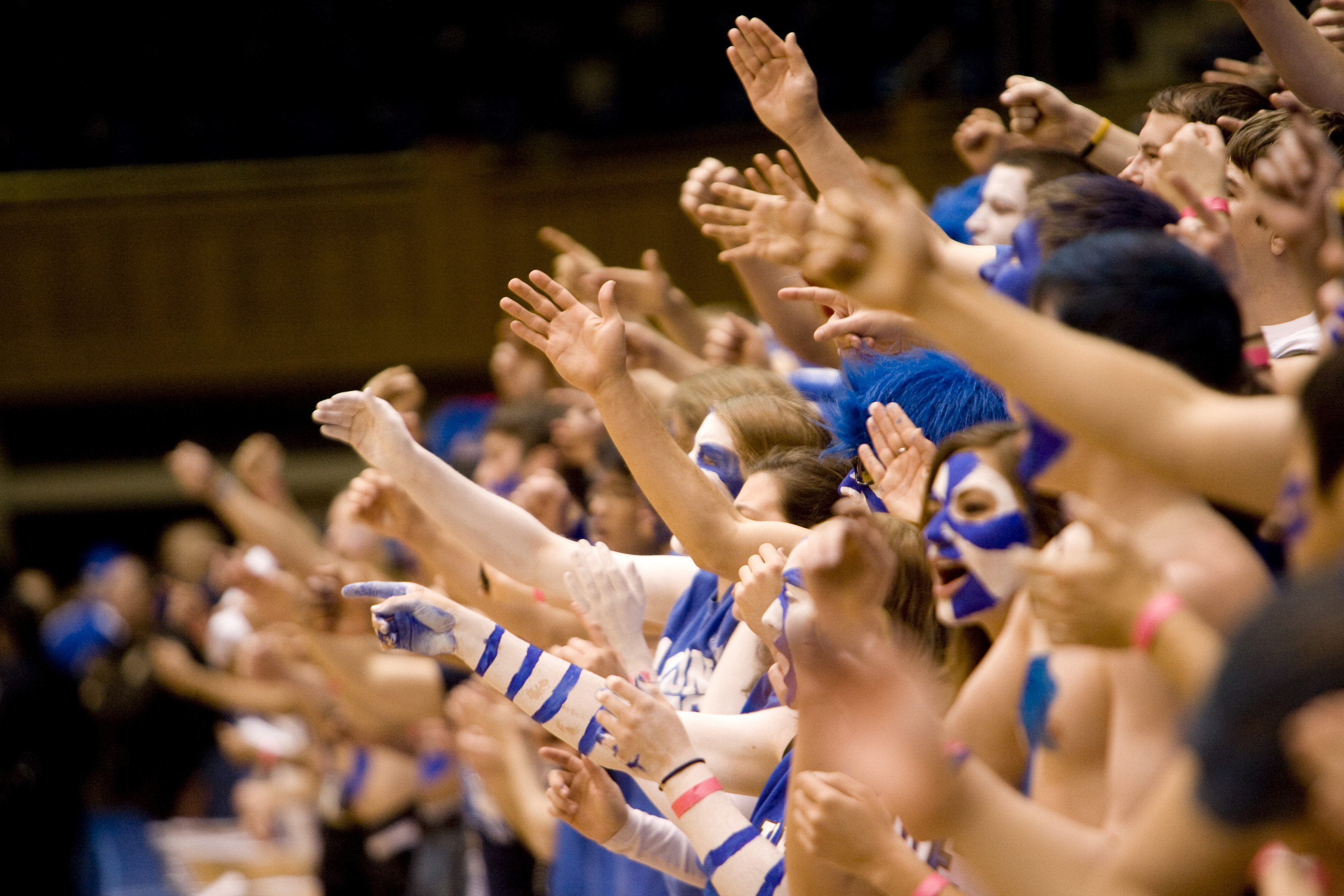 crowd of students in the stands, dressed in duke blue cheering and waving