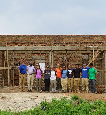 students and faculty posing together in front of a house being built
