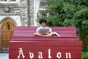 duke student doing homework on a tall bench outside on West Campus