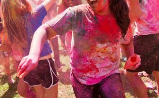 students covered in colorful powder laughing and playing holi on a field in the daytime