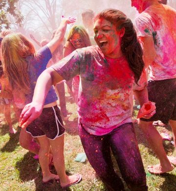 students covered in colorful powder laughing and playing holi on a field in the daytime